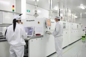 Workers in cleanroom suits monitoring high-tech equipment in a modern manufacturing facility, showcasing precision and automation in industrial processes