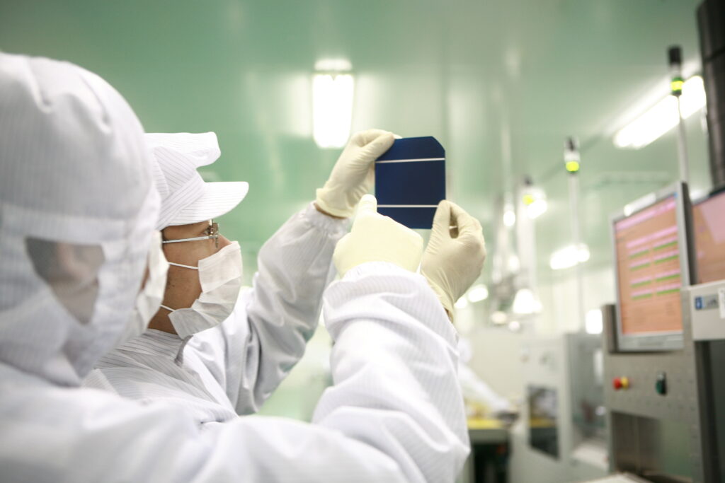 Technicians in cleanroom suits inspecting a solar cell under bright lighting in a high-tech manufacturing environment, showcasing quality control in photovoltaic production.